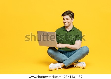 Full body young programmer smart happy IT man he wears green t-shirt casual clothes sitting hold use work on laptop pc computer isolated on plain yellow background studio portrait. Lifestyle concept
