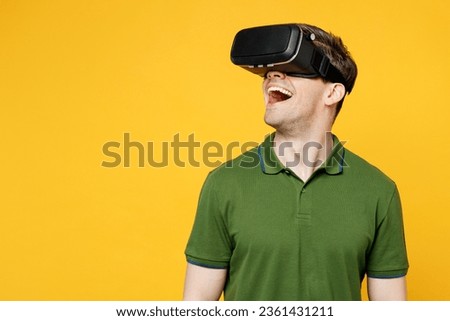 Young surprised amazed cheerful fun cool caucasian happy man wears green t-shirt casual clothes watching in vr headset pc gadget isolated on plain yellow background studio portrait. Lifestyle concept