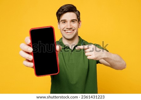Young happy man wears green t-shirt casual clothes hold in hand use point finger on close up mobile cell phone with blank screen workspace area isolated on plain yellow background. Lifestyle concept