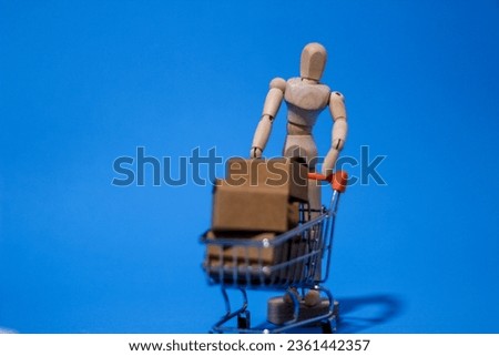 Wooden mannequin pushing shopping cart full of carton shipping boxes ready for delivery representing consumerism.