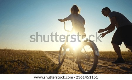 dad teaches daughter to ride a bike. happy family childhood dream concept. father and little daughter learn to ride bike silhouette in the park. happy family goes in for sunlight sports outdoors Royalty-Free Stock Photo #2361451151