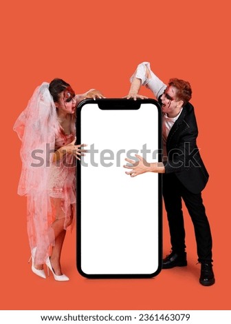 Young wedding zombie couple and big mobile phone with empty screen on orange background. Halloween celebration