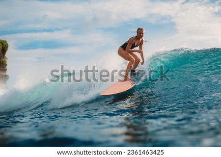 Attractive blonde surf girl riding on surfboard in ocean during surfing. Surfer on blue wave