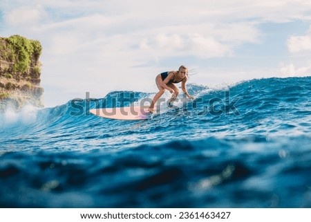Attractive blonde surf girl riding on surfboard in ocean during surfing. Surfer on blue wave