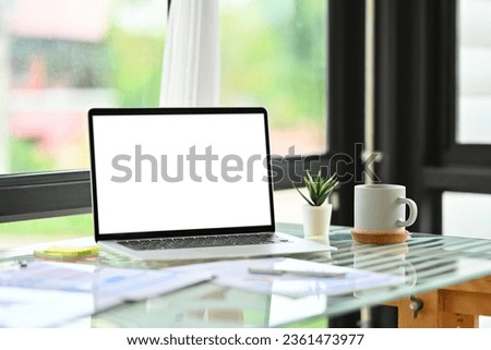 Front view of laptop with white blank display, coffee cup, pencil holder and books on office desk