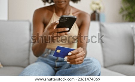 African american woman make photo to credit card by smartphone sitting on sofa at home