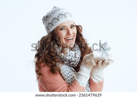 Hello winter. Portrait of smiling modern female in sweater, mittens, hat and scarf against white background with snowflake.