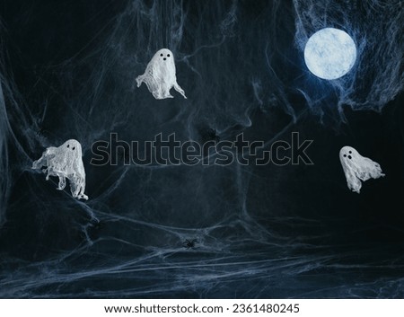 Halloween dark background with ghosts, glowing moon and a spider web with copy space. Image for montage or display your products. Ghosts made of gauze and starch. Halloween decor.