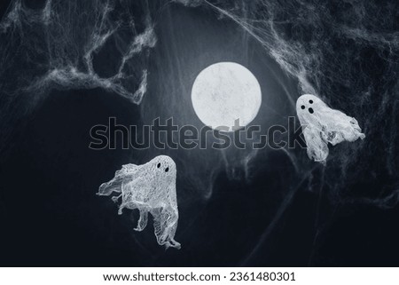 Ghosts of gauze on a dark background with glowing moon and spider web. Creative DIY Halloween decor. Halloween greeting card. Copy space. Royalty-Free Stock Photo #2361480301