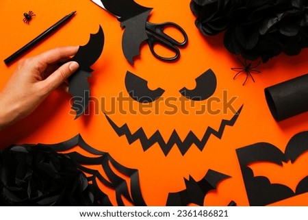 Female hand, paper bats, eyes and mouth on orange background, top view