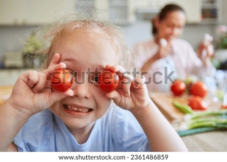 Portrait of cute blond girl holding ripe cherry tomatoes in kitchen at home