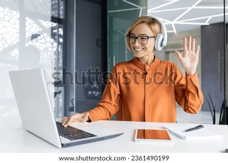 Young joyful woman at workplace listens to music in headphones, businesswoman dances and sings, sitting at work table inside office, female programmer well done successf technical project celebrates. Royalty-Free Stock Photo #2361490199