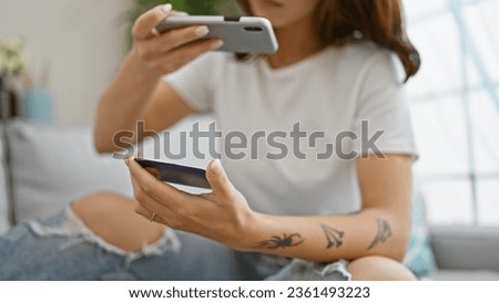 Young woman make photo to credit card by smartphone sitting on sofa at home