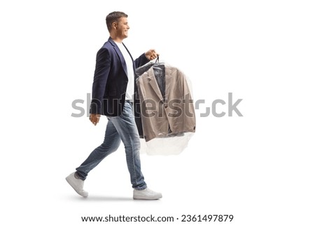 Full length profile shot of a man carrying suit on a hanger with a plastic dry cleaning bag isolated on a white background Royalty-Free Stock Photo #2361497879