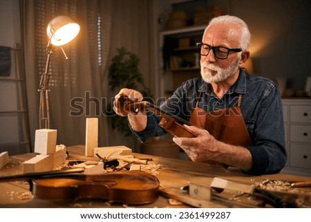 Senior carpenter craftsman carving wood and making violin instrument Royalty-Free Stock Photo #2361499287