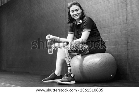 Confident woman with artificial leg sits relax after exercising in fitness gym. Prosthetic limb strengthen physical injury amputee. Asian female with mechanical prosthesis leg workout for wellbeing.