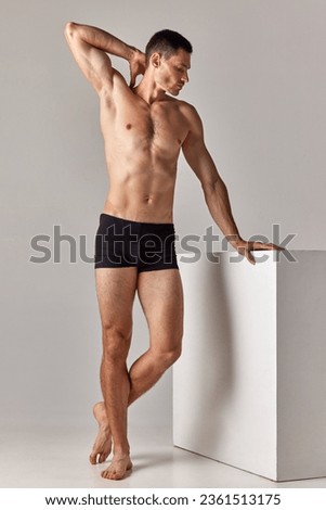 Full-length image of handsome, shirtless man with muscular body posing in underwear against grey studio background. Concept of men's health and beauty, body care, fitness, wellness, ad Royalty-Free Stock Photo #2361513175
