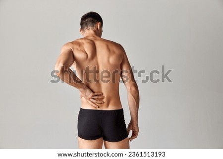 Back pains. Muscular man standing in underwear and holding his back against grey studio background. Medical treatment. Concept of men's health and beauty, body care, fitness, wellness, ad Royalty-Free Stock Photo #2361513193