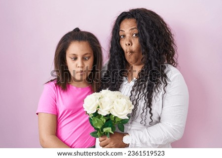 Mother and young daughter holding bouquet of white flowers making fish face with mouth and squinting eyes, crazy and comical. 