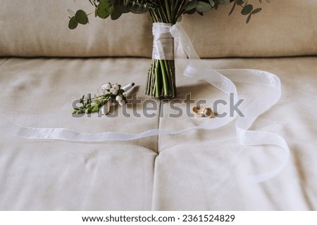Wedding accessories and details, gold rings, a beautiful bouquet of flowers with a ribbon lie on a beige sofa. Close-up photography, portrait. Royalty-Free Stock Photo #2361524829