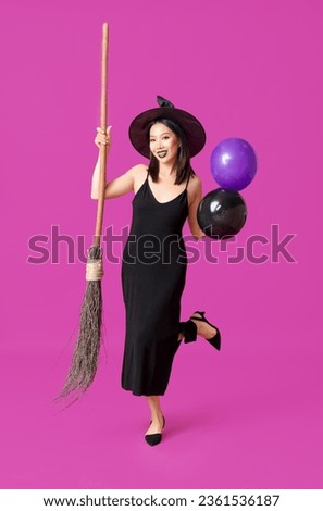 Young Asian woman dressed for Halloween as witch with balloons on color background