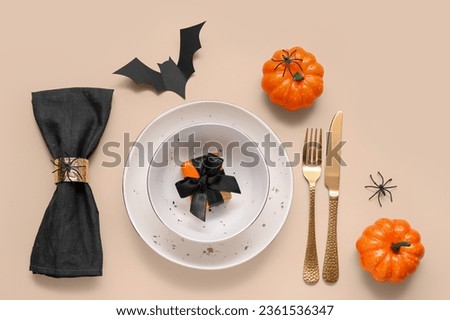 Festive table setting with Halloween pumpkins and bat on beige background