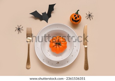 Festive table setting with Halloween pumpkins and bat on beige background