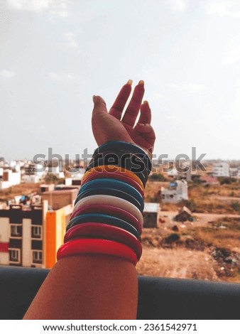 This picture depicts a girl hand with full of bangles that is colourful extended towards the sky.