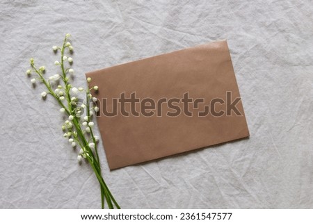 Blank greeting card, invitation and envelope mockup. Minimal floral arrangement with white lilies of the valley. Flat lay, top view. Happy mother's day, birthday, wedding composition.