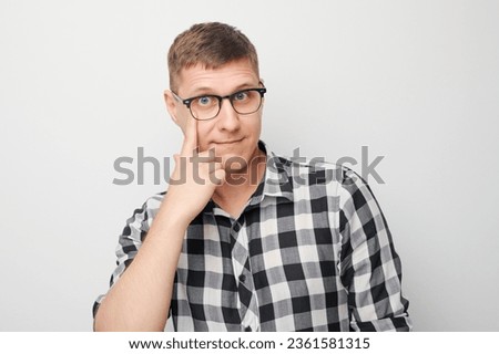 Portrait of young male pointing finger at spectacles on face isolated on white studio background. Vision check and loss of sight, search concept, eyewear shop
