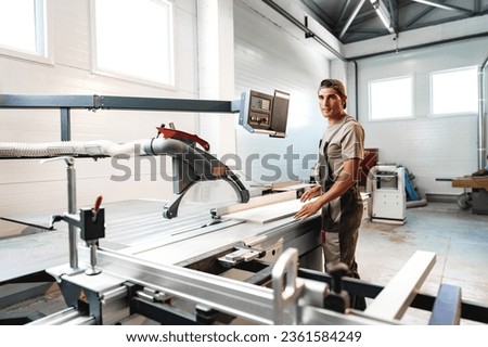 Young carpenter cutting a piece of wood in using a circular saw in furniture factory Royalty-Free Stock Photo #2361584249