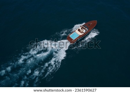 Luxury wooden big speedboat fast moving on dark water top view. Expensive wooden big boat with people moving on the water aerial view. Boat movement on the water. Royalty-Free Stock Photo #2361590627