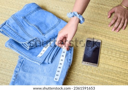 Woman hand attaching size labels on blue jeans on korai grass mat background. Preparation for livestream selling online or vlogging. 