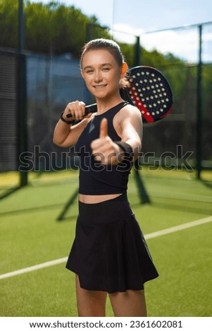 Padel tennis player with racket. Happy smiling girl athlete with thumbs up on court outdoors. Sport concept. Download a high quality photo for the design of a sports app or web site.