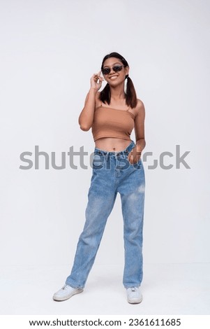 A confident Filipino woman in her late teens or early 20s. Wearing a brown top and loose fitting jeans. Isolated on a white backdrop. Royalty-Free Stock Photo #2361611685