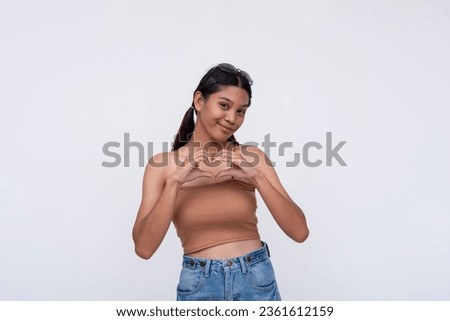 A lovely Filipina makes a heart shape gesture with both hands. Isolated on a white backdrop. Royalty-Free Stock Photo #2361612159