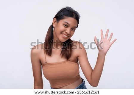 A friendly Filipina waving hi. A friendly young woman waving her hand. Isolated on a white backdrop. Royalty-Free Stock Photo #2361612161
