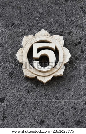 NUMBER 5 FIVE CARVED OUT OF SANDSTONE IN A CIRCULAR FLOWER DESIGN - Light colored detailed stylish decorative carved numbered sign with dark gray black textured granite brick background