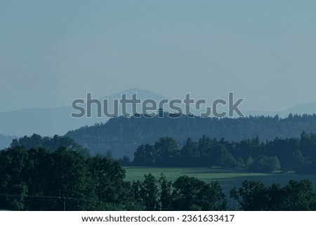 Sudetes foreland. The undulating terrain is covered with farmlands, meadows and forests. On the horizon you can see the peaks of the Sudetes Mountains, hidden in the fog and very blurred. Royalty-Free Stock Photo #2361633417