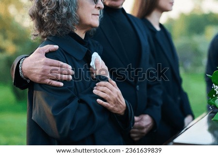 Hand of mature man on shoulder of his wife or sister with handkerchief lamenting passes away relative or family member during funeral service Royalty-Free Stock Photo #2361639839