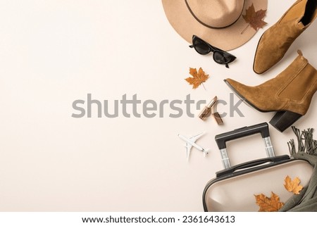 Feminine autumnal air journey vision. Top-view of mini plane, classy felt hat, cat-eye sunglasses, scarf, western boots, suitcase, maple leaves, lipstick on subtle pastel backdrop, room for text or ad Royalty-Free Stock Photo #2361643613