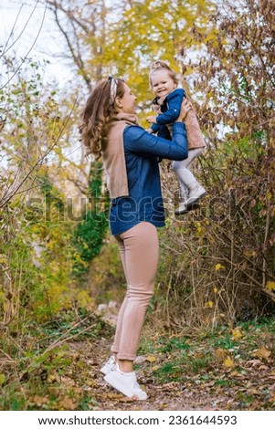 Side view: Mom throws the baby up. Time together in the autumn park mother and daughter. Mom 28-35 years old, toddler 1-2 years old. Concept: family, mother's day, happy childhood, motherhood Royalty-Free Stock Photo #2361644593
