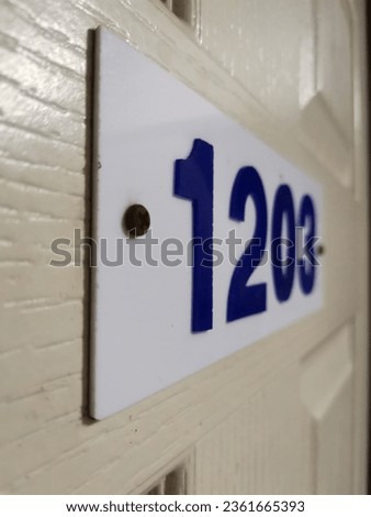 The image of a door with the number 1203 attached to it is located at the front entrance. The door's wooden surface is in a rice color, and there is a sign attached to the doorframe.