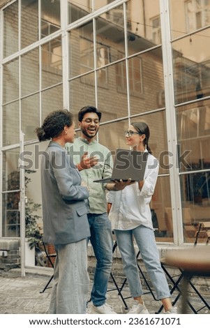 Cheerful coworkers discuss the project while use laptop standing on cafe terrace background Royalty-Free Stock Photo #2361671071