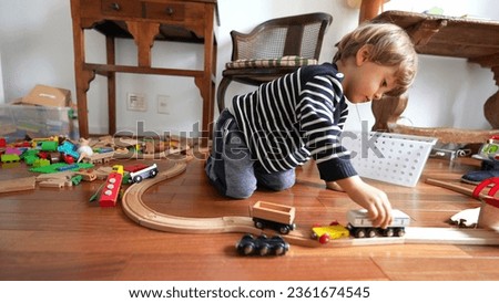 Small boy playing with car toys on hardwood floor. Child plays by himself with traditional toy on tracks Royalty-Free Stock Photo #2361674545