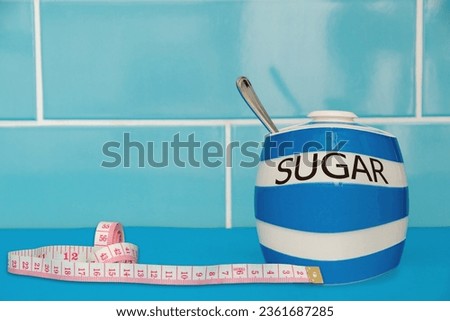 Weight loss Sugar concept. A fat sugar pot with a tape measure by its side. A blue themed picture with good copy space. Diet and lifestyle picture.