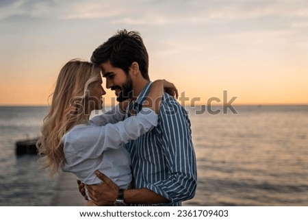 Lovely couple bonding at the beach in summer. Romantic male and female looking each other into eyes during the sunset. Beautiful couple in love standing face to face. Royalty-Free Stock Photo #2361709403