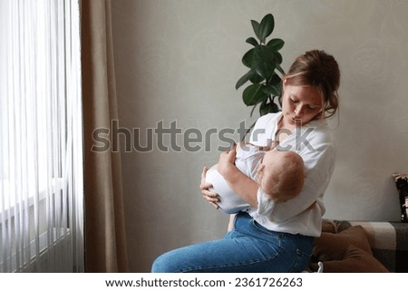 Young mother and baby daughter, son are having fun at home by window together. Beautiful mom throws her adorable newborn infant up and catches. Concept of childhood, new life, parenthood. Mothers day.