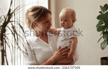 Loving tender young mum holding adorable cute baby girl daughter hugging small kid. Happy affectionate mother cuddling with infant child boy son standing at home by window. Happy motherhood concept.