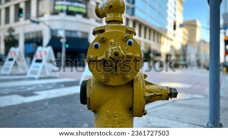 Wide, landscape photo of yellow fire plug (fire hydrant) with googly eyes on a street corner in Downtown Los Angeles, CA, day time Royalty-Free Stock Photo #2361727503